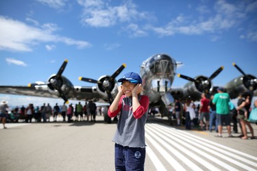 Ming Chen, 10, plugs his ears as a CF-18 flies overhead on the main runway with a WW II b-17 bomber Sentimental Journey in the background during the Wings Over Springbank air show at Springbank Airport west of Calgary on July 19, 2015.