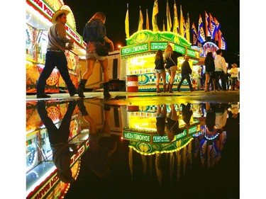 Stampede goers are reflected in a puddle left over from the afternoon's hail storm as the midway slowly winds down near midnight on July 4, 2015.