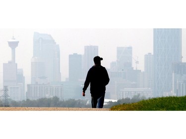 Charlie Coffin walks along the pathway above Max Bell Centre with the smoke shrouded downtown in the distance in Calgary Monday August 24, 2015.