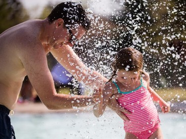 Craig MacLellan, left, holds his daughter Sophie, 4, under a mushroom shaped sprinkler at the Bowview Outdoor Pool in Calgary on Monday, Aug. 10, 2015.