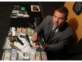 Calgary Police Staff Sgt. Martin Schiavetta poses with weapons, drugs and money seized from a recent drug investigation in Calgary on August 4, 2015.