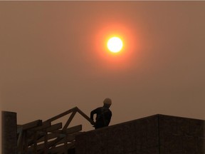 A construction worker in Bridgeland is silhouetted by the recent smoke shrouded sun.