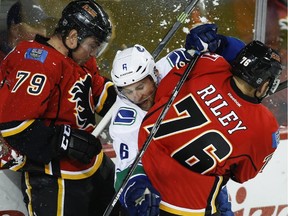 Vancouver Canucks' Yannick Weber, centre, from Switzerland, gets sandwiches between Calgary Flames' Michael Ferland, left, and Blair Riley during NHL pre-season hockey action in Calgary, Friday, Sept. 25, 2015.