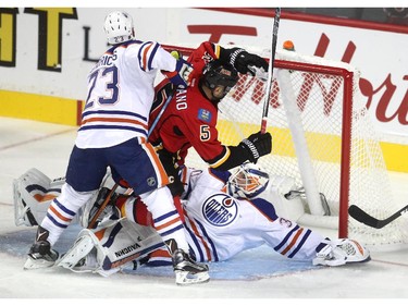 Calgary Flames defenceman Mark Giordano crashed into Edmonton Oilers goalie Ben Scrivens, right, as he was checked by Oilers left winger Matt Hendricks during the first period of a split squad preseason NHL game at the Scotiabank Saddledome on September 21, 2015.