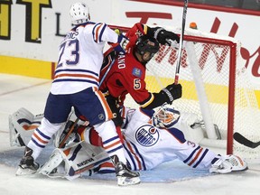 Calgary Flames defenceman Mark Giordano crashed into Edmonton Oilers goalie Ben Scrivens, right, as he was checked by Oilers left winger Matt Hendricks during the first period of a split squad preseason NHL game at the Scotiabank Saddledome on Monday.