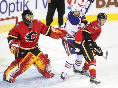 Calgary Flames goalie Jonas Hiller, left, guarded his crease as Flames defenceman Brett Kulak, right, and Edmonton Oilers left winger Benoit Pouliot fought for position during the first period of a split squad preseason NHL game at the Scotiabank Saddledome on September 21, 2015.