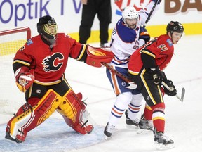 Calgary Flames goalie Jonas Hiller, left, guards his crease as Flames defenceman Brett Kulak, right, and Edmonton Oilers left winger Benoit Pouliot fight for position during the first period of a split squad preseason NHL game at the Scotiabank Saddledome on Monday.