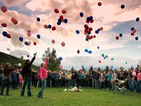 Marc Ernst and Katie Matthews raise their arms as pink and blue balloons are released at a field west of the Isabelle Sallon School in Blairmore on Friday evening. More than 200 people gathered to remember Terry Blanchette and his two-year-old daughter, Hailey Dunbar-Blanchette, who were murdered in the Crowsnest Pass community earlier this week.