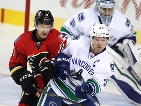 Mikael Backlund of the Calgary Flames jousts with Vancouver Canucks captain Henrik Sedin in front of goalie Ryan Miller during the season opener.