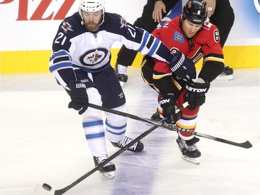 Calgary Flames defenceman Dennis Wideman reached for the puck against Winnipeg Jets left winger Thomas Raffl during first period NHL action at the Scotiabank Saddledome on October 3, 2015.