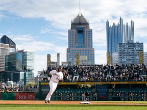 A Pittsburgh Pirates player rounds third base with the city skyline behind him.