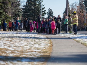 A firefighter helps load evacuated school children on to city buses after emergency crews were called in for a possible carbon monoxide leak at Woodlands elementary school in Calgary on Nov. 4, 2015.