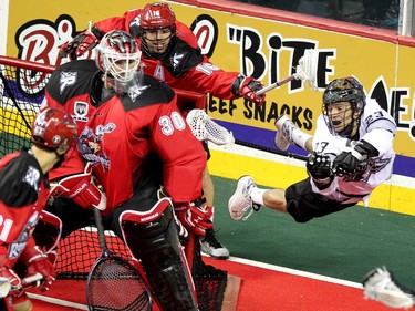 Calgary Roughnecks defenceman Mike Carnegie, background, tried to stop a flying Edmonton Rush transition Jarrett Davis as he stuffed the ball into the net of Roughnecks goalie Mike Poulin during NLL game action at the Scotiabank Saddledome on January 24, 2015.