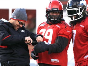 Calgary Stampeders defensive lineman Charleston Hughes gets on-field adjustments to a bandage on his cast while laughing with fellow lineman Junior Turner at McMahon Stadium on Thursday.
