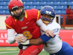 Dinos player Andrew Buckley, left, pulls a UBC player along for the ride at  McMahon Stadium in Calgary on Friday, Sept. 4, 2015. The University of Calgary Dinos football team hosted the University of British Columbia Thunderbirds in the home opening game of the 2015 season.
