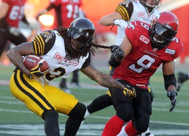 Calgary Stampeders Jon Cornish gives a tug on the Hamilton Tiger-Cats Johnny Sears Jr. during their season opener at McMahon Stadium, on June 26, 2015. (Christina Ryan/Calgary Herald)