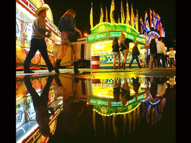 Stampede goers are reflected in a puddle left over from the afternoon's hail storm as the midway slowly winds down near midnight on July 4, 2015.