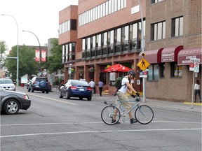 A  cyclist walks his bike through a crosswalk on Kensington Road.