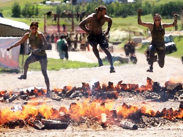 Kaila Maddalo, left, Mathew Dorsey and Amanda Blais jump the Pyromania at the Rugged Maniac run Saturday July 18, 2015 at Rocky Mountain Show Jumping. Hundreds of adventurers ran, climbed and slogging through a 5 kilometre course of ropes, towers, mud and fire.