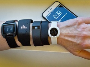 Fitness trackers, from left, Basis Peak, Adidas Fit Smart, Fitbit Charge, Sony SmartBand, and Jawbone Move, are posed for a photo next to an iPhone. The devices are adding features as their price drops.