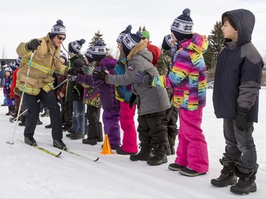 A firefighter high-fives kids as he skis by at Mount View School in Calgary, Alta., on Tuesday, Jan. 26, 2016. The Calgary Fire Department and Calgary Police Service, along with a pair of Olympians, went head-to-head in a relay race for an announcement by AltaGas to support Cross Country Ski de Fond Canada's Ski at School program for the next three years. Lyle Aspinall/Postmedia Network