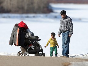Sayed Ali watches his two-year-old son Ibrahim take tentative steps as the family enjoys the trail at South Glenmore Park on another day of 14 degree Celcius temperatures in Calgary. (Ted Rhodes/Postmedia)