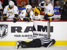 Nashville Predators' players look over the bench at linesman Don Henderson after he was hit by Calgary Flames' Dennis Wideman during second period NHL hockey action in Calgary, Wednesday, Jan. 27, 2016. Wideman's suspension has been reduced from 20 games to 10. THE CANADIAN PRESS/Jeff McIntosh