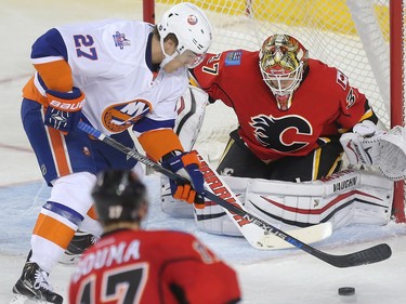 Calgary Flames goalie Joni Ortio eyes the loose puck on the stick of Anders Lee of the New York Islanders in the third period of their 2-1 overtime loss at the Saddledome Thursday night February 25, 2016.