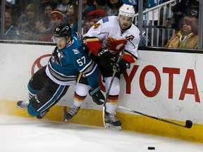 Calgary Flames defenceman Kris Russell (4) is checked into the boards by San Jose Sharks center Tommy Wingels (57) during the first period of an NHL hockey game in San Jose, Calif., Thursday, Feb. 11, 2016.