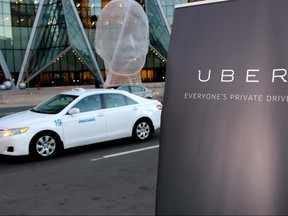 Taxi drives by a sign announcing the kickoff of Uber ride service in Calgary, Ab., on Thursday October 15, 2015. Mike Drew/Postmedia Network