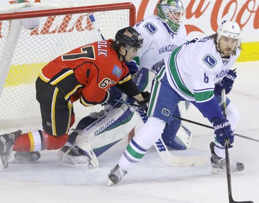 Calgary Flames Michael Frolic scrambles to get out from behind Vancouver Canucks goalie Jacob Markstrom as Canucks Christopher Tanev stands guard in NHL hockey action at the Dome in Calgary, Alta. on Friday February 19, 2016. Mike Drew/Postmedia