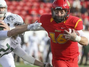 Calgary Dinos' quarterback Jimmy Underdahl runs with the ball and pushes back a tackle during playoff action against the Sask Huskies at McMahon Stadium in Calgary, on November 7, 2015.