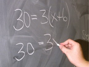 A teacher writes a math problem on a blackboard.