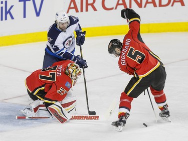 Mark Giordano of the Calgary Flames swats a puck away from Drew Stafford of the Winnipeg Jets near goalie Joni Ortio in Calgary, Alta., on Wednesday, March 16, 2016. The Flames won 4-1. Lyle Aspinall/Postmedia Network