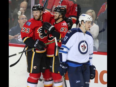 Winnipeg Jets Adam Lowry skates back to the bench as Michael Frolik of the Calgary Flames celebrates with teammate Jakub Nakladal after scoring during NHL hockey in Calgary, Alta., on Wednesday, March 16, 2016. AL CHAREST/POSTMEDIA