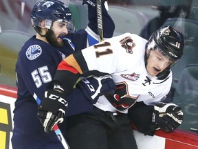 Beck Malenstyn of the Calgary Hitmen in taken into the glass behind the Saskatoon Blades net by defender Colton Waltz in the third period at the Scotiabank Saddledome on Tuesday night.