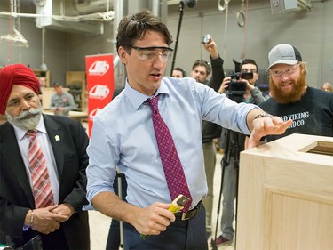 Prime Minister Justin Trudeau helps carpentry student Tristram Reeves-Rood with a project as he's watched by MP Darshan Kang at SAIT Polytechnic in Calgary, Alta., on Tuesday, March 29, 2016. Trudeau was part of a roundtable discussion on employment insurance at the Kerby Centre before touring a carpentry lab at SAIT Polytechnic.