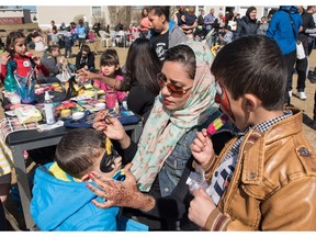 Abeer Merali, a henna and makeup artist, transforms a young boy into Batman at a potluck for Syrian refugees and their new neighbours in Calgary on Sunday, April 3, 2016.