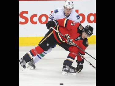 Sam Bennett of the Calgary Flames eyes a loose puck while being held up by Brendan Gaunce in the second period against the Vancouver Canucks at the Saddledome Thursday night April 7, 2016.  (Ted Rhodes/Postmedia)