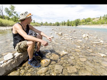 A young man who would only be identified as 'Show Biz' takes a break after building cairns, or 'living rocks', in the Bow River at Prince's Island Park in downtown Calgary, Alta., on Wednesday, May 18, 2016. Show Biz says his cairns serve a variety of artistic, therapeutic and calming purposes, his favourite of which is creating a sense of welcomeness and community in an area too often hit with petty crime. Lyle Aspinall/Postmedia Network