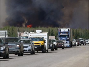 A convoy of evacuees drives south as flames and smoke rise along the highway near Fort McMurray on May 6.