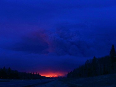 A plume of smoke hangs in the air as forest fires rage on in the distance in Fort McMurray, Alberta on May 4, 2016. Numerous vehicles can be seen abandoned on the highways leading from the raging forest fires in Fort McMurray and neighbouring communities have banded together to offer support in the form of food, water, and gasoline.