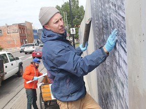 Daniel J. Kirk, right, of Blank Page Studio, along with Ryan McClure Scott, applies a panel to the hoarding around a development on 9th Avenue SE in Inglewood Friday May 20, 2016. The panel, part of a project called Studious, is one of a variety depicting stories from the history of Inglewood, this one representing geological time on the banks of the Bow River. The project is on the site of the former Frosst Books, Inglewood Art Supplies and the former bottle depot. It was commissioned by Jim Hill.