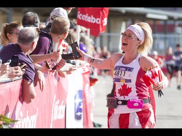 Courtney Stang gives high-fives and mini-flags while completing the half-marathon during the Calgary Marathon at the Stampede Grounds in Calgary, Alta., on Sunday, May 29, 2016. There were 5k, 10k, 21.1k, 42.2k and 50k distances in the race, including the half-marathon national championships. Lyle Aspinall/Postmedia Network