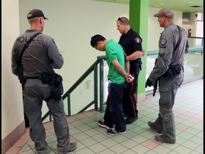 A blood covered man is escorted in handcuffs form a stabbing incident in the Perpetual Wellness Chinese Medicine Centre on Thursday June 16, 2016