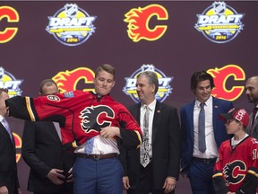 Matthew Tkachuk, sixth overall pick, pulls on his sweater as he stands on stage with members of the Calgary Flames management team at the NHL draft in Buffalo, N.Y. on June 24, 2016.