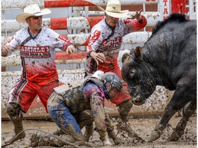 Bullfighters Scott Byrne, left, Scott Waye moves in to protect Clayton Foltyn of Winnie, Tx., after he bucked off Canadian Outlaw into the mud at the Stampede Rodeo at the Calgary Stampede in Calgary, Ab., on Friday July 15, 2016.