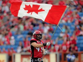 Calgary Stampeders Alex Singleton carries the flag at the start of their game against the Winnipeg Blue Bombers during CFL action at McMahon Stadium in Calgary, Alta.. on Friday July 1, 2016. Leah hennel/Postmedia