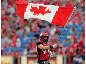 Calgary Stampeders Alex Singleton carries the flag at the start of their game against the Winnipeg Blue Bombers during CFL action at McMahon Stadium in Calgary, Alta.. on Friday July 1, 2016.