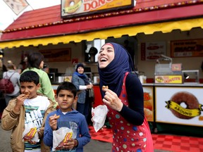 Syrian refugee Batoul Abboud, 17, right, tries her first mini donut at the Calgary Stampede in Calgary, Alta., on Wednesday July 13, 2016. Leah Hennel/Postmedia